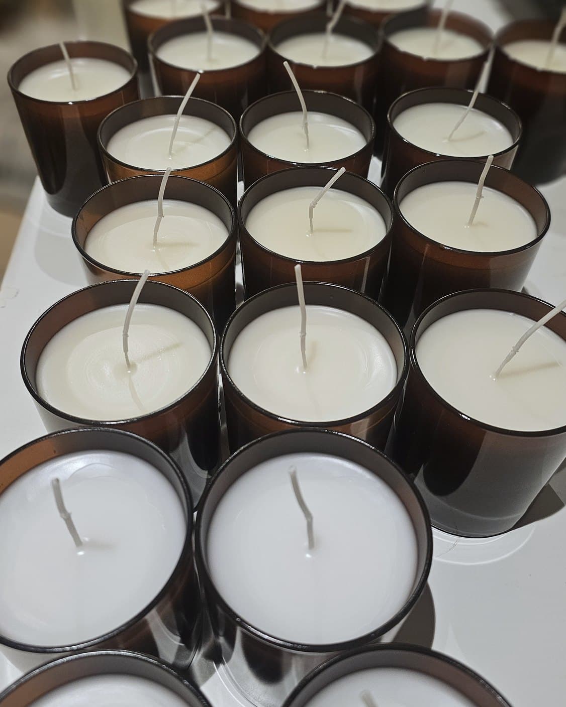 Rows of freshly poured candles in amber glass jars, the wax set white, each wick standing in the centre.
